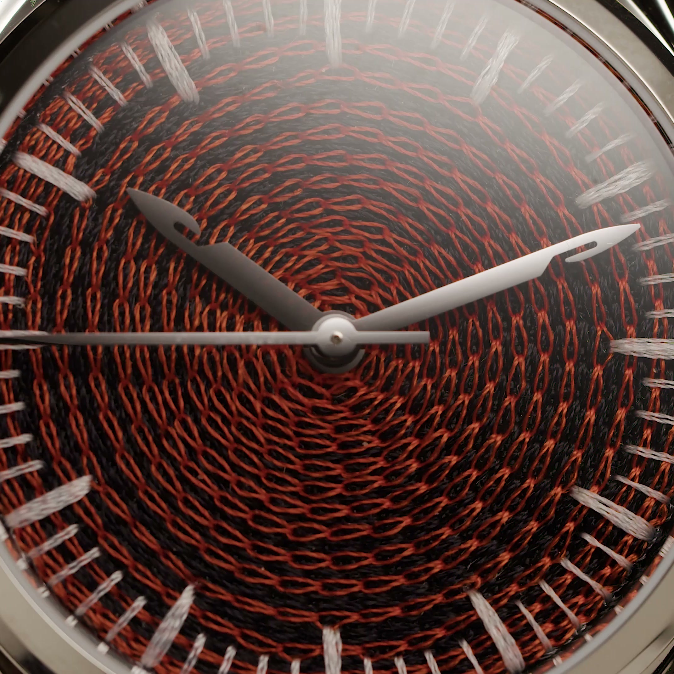 Close view of the CORNELY dial: a spiral of raised red and black chain-stitch loops, needle-shaped steel hands across it