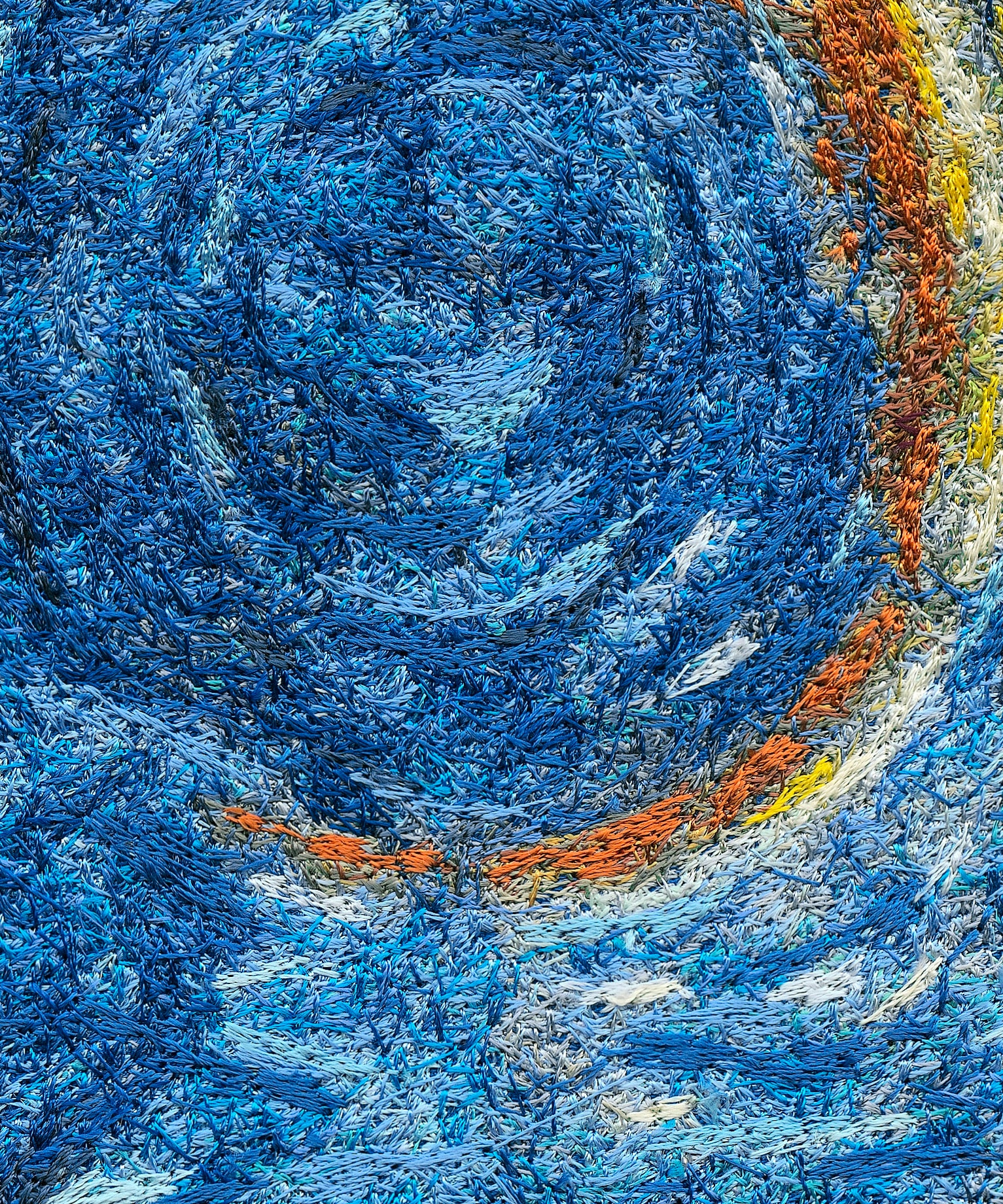 Embroidery under a macro lens, close enough to see each individual stitch: swirling blue thread with an arc of orange and yellow stitches