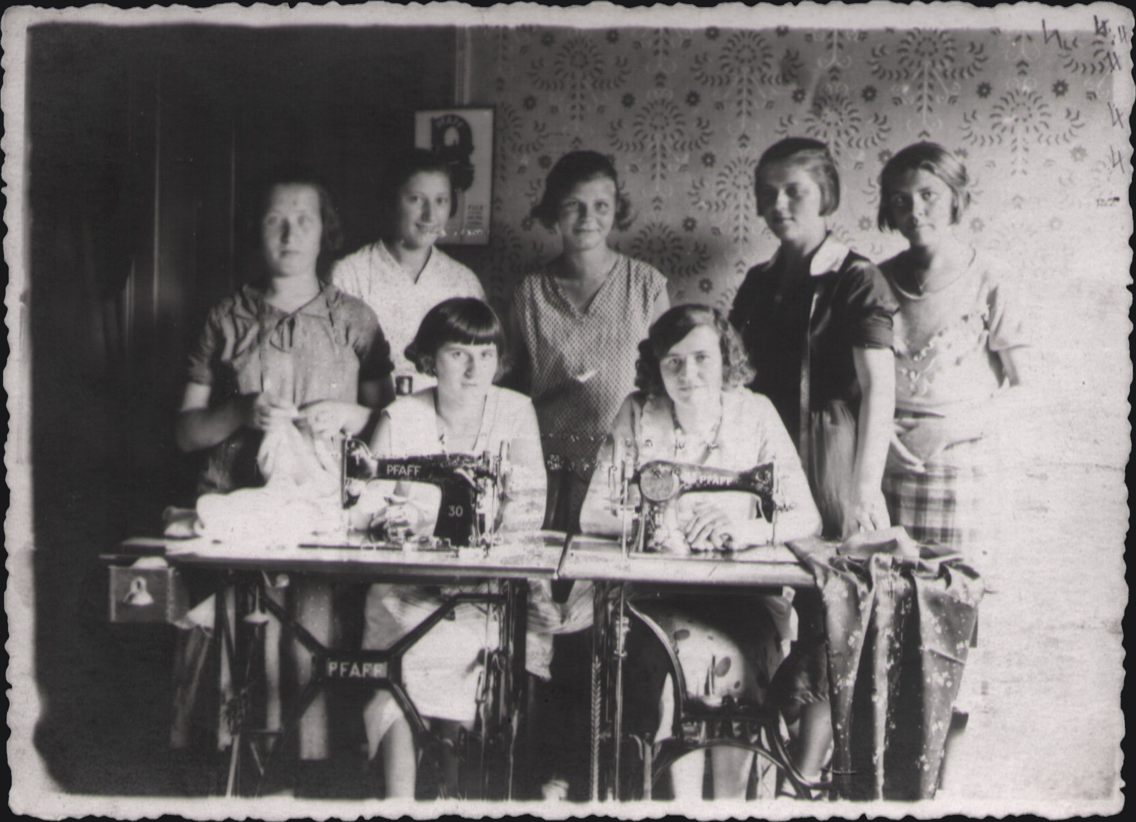 Black-and-white photograph from the founding years: seven young women around two Pfaff sewing machines, 