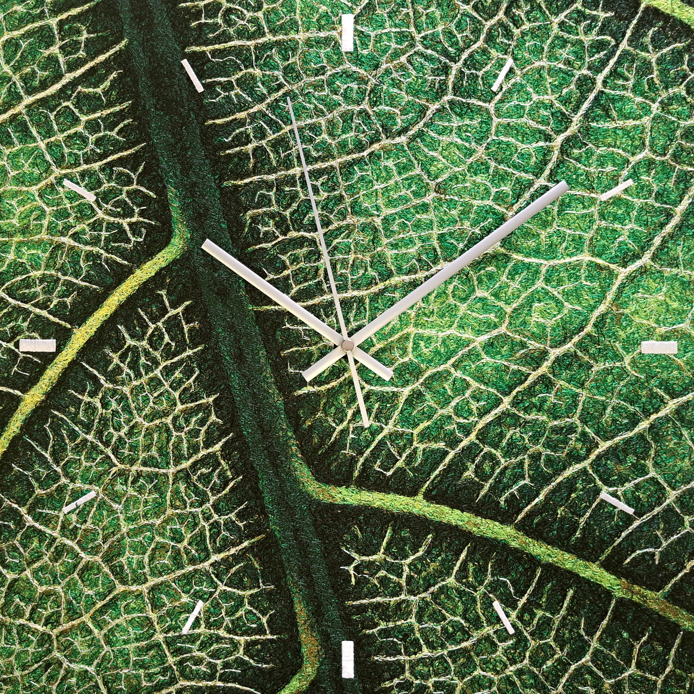 A square wall clock whose embroidered dial is a photorealistic close-up of a green leaf and its veins, with white markers and slim white hands