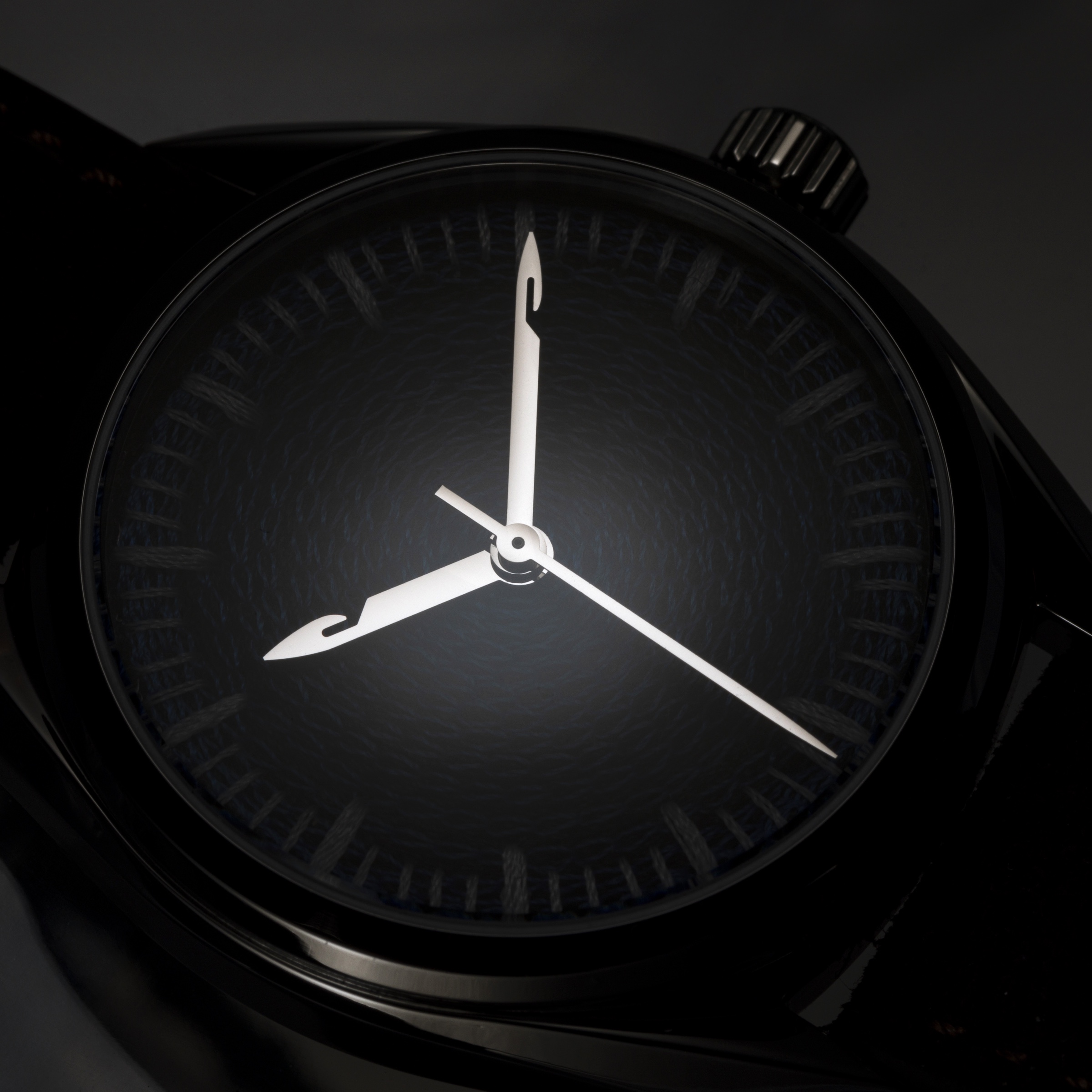 Chenille-embroidered watch dial emerging from darkness, needle-shaped hands catching the light